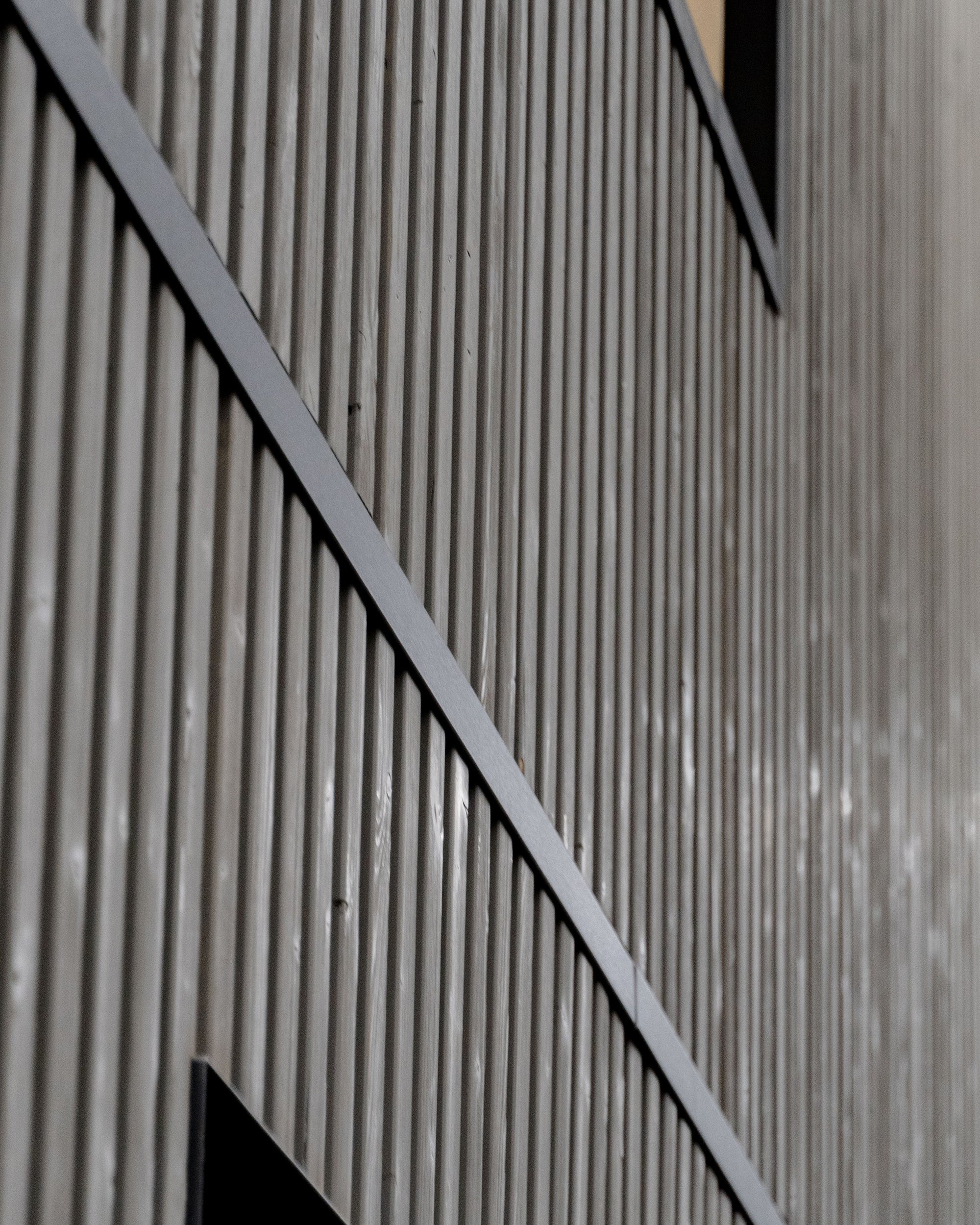 Modern building facade with vertical Aluwood acoustic facade panels, black-framed windows, and geometric lines for a minimalist Nordic architectural style.